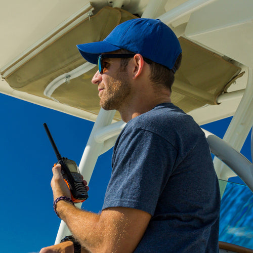 Man on a boat grips a handheld marine radio with a blue sky background
