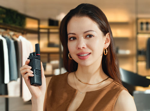 A retail employee holds up a black walkie-talkie in a retail store setting