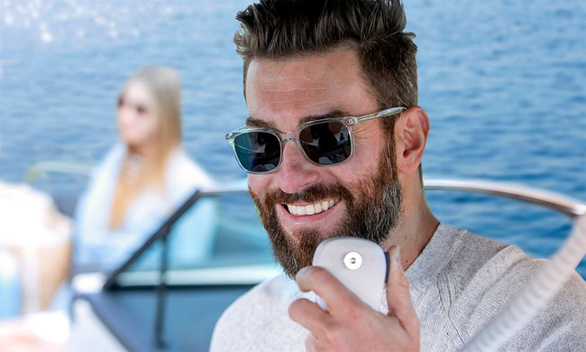 Man with sunglasses smiling while holding the microphone of a Cobra BlueBound 1350 marine radio on a boat with a passenger in the background