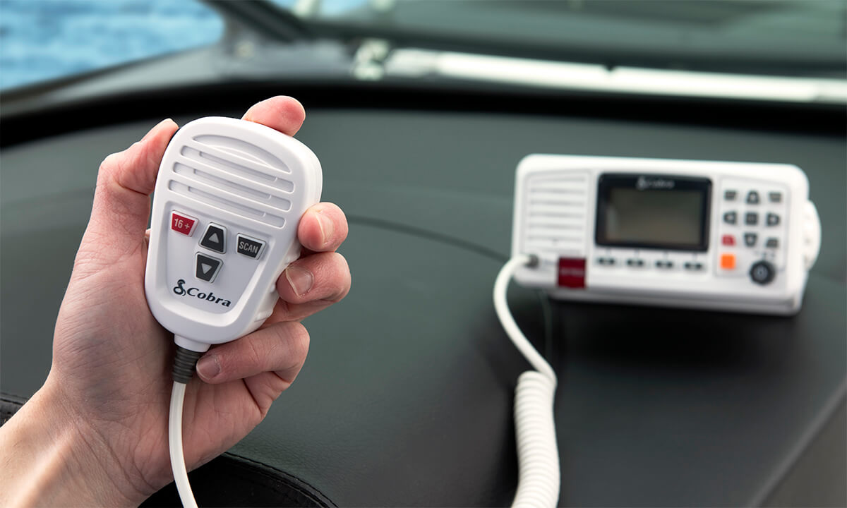 Hand holding a white Cobra BlueBound 1350 marine radio with boat dashboard in the background