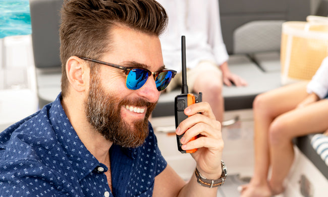 Man wearing sunglasses on a boat listens to Cobra BlueBound 150 VHF marine radio