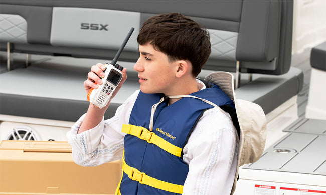 Young man in a blue lifejacket holding a white Cobra BlueBound 350 VHF marine radio on a boat