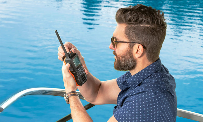 Man on a boat adjusting the dial on a black Cobra BlueBound 650 marine radio