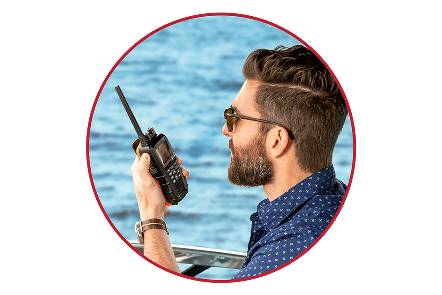 Man on a boat using a black Cobra BlueBound 650 marine radio with open water in the background