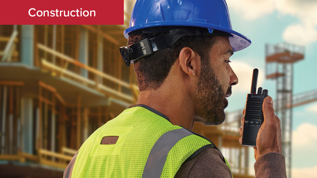 A construction worker in hardhat and high visibility vest uses Cobra PX650 Business Walkie Talkie at a jobsite