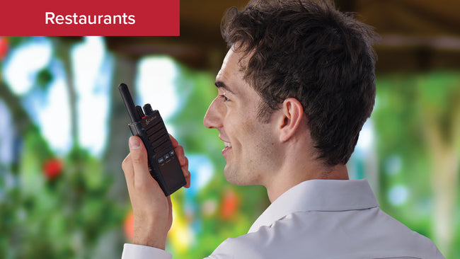 A male restaurant staff member in an outdoor seating area calls to back of house with the Cobra PX650 business radio
