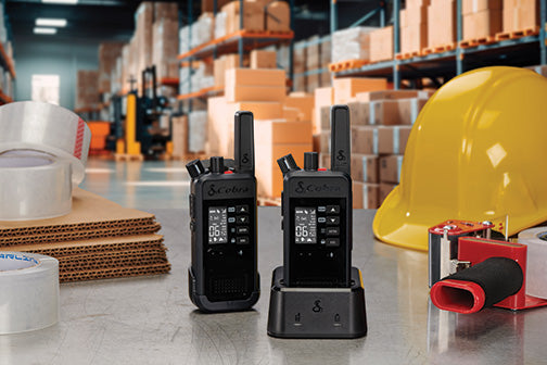 Two Performa walkie-talkies on a table with a hard hat and tape in a warehouse setting.